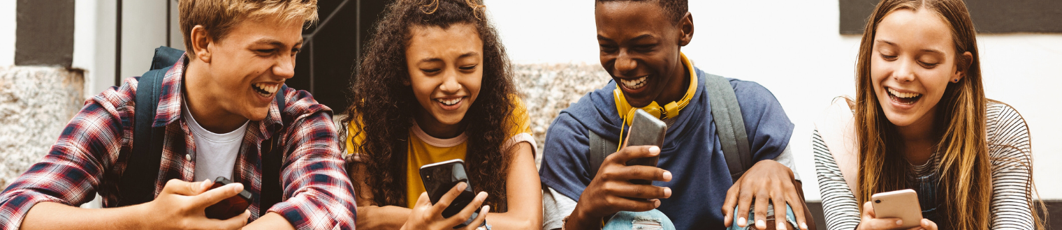 2 teenage boys and 2 teenage girls smiling while on their smartphones.